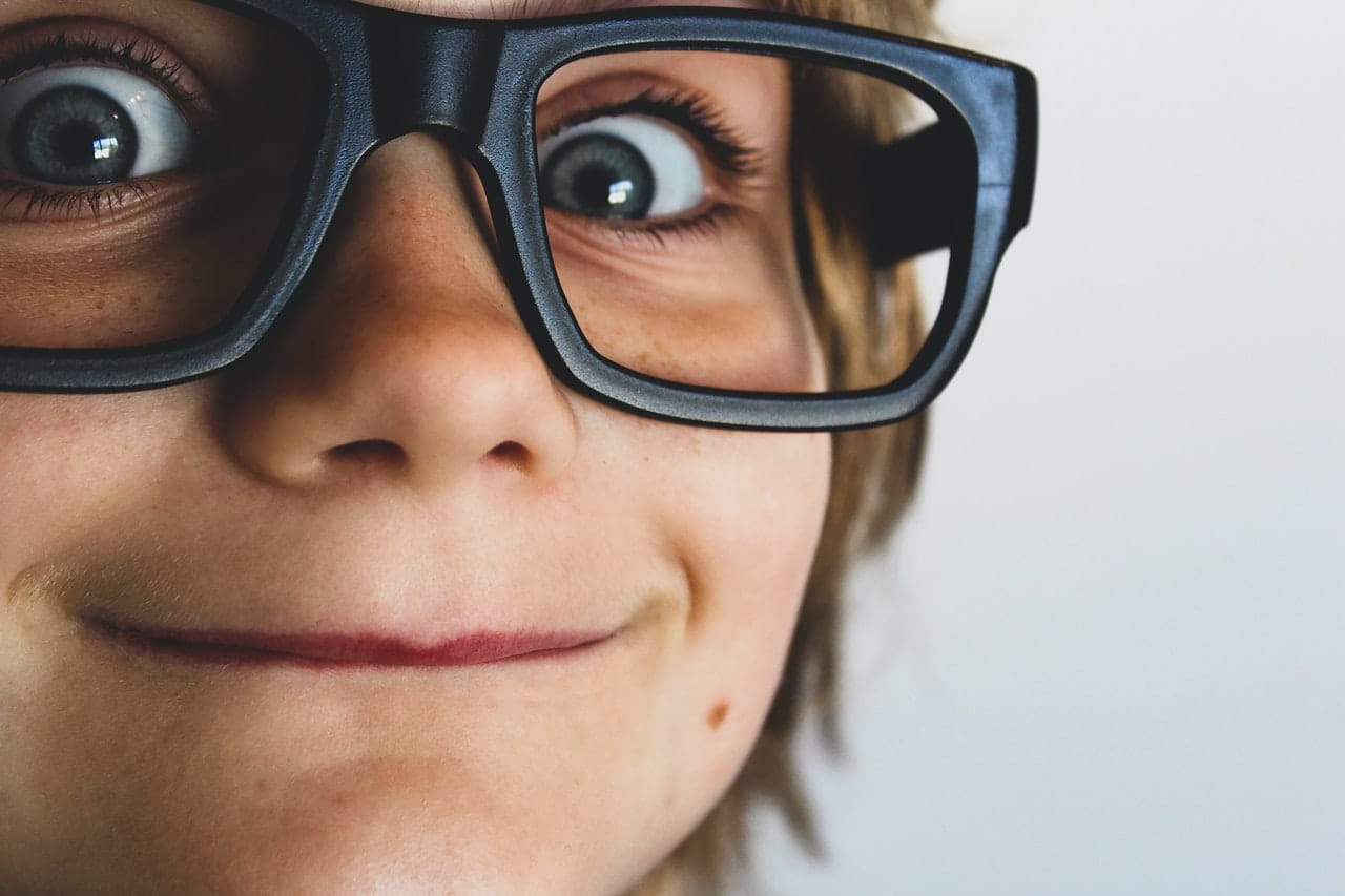 Ein Kind mit blitzenden Augen hinter einer zu grossen Brille 